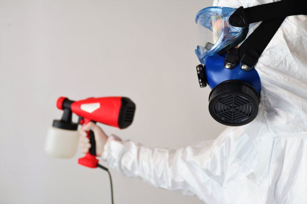 A photo of a person wearing a PPE suit and mask and holding pest control equipment