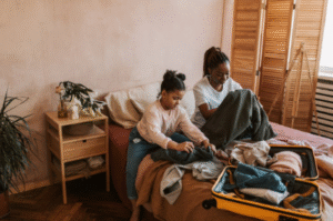 A packed suitcase sitting on a bed beside winter clothes and luggage tags