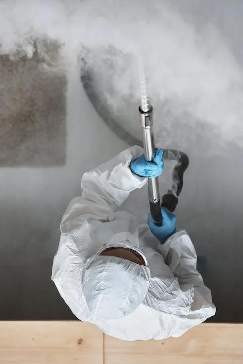 An image of an exterminator wearing a protective suit and holding equipment